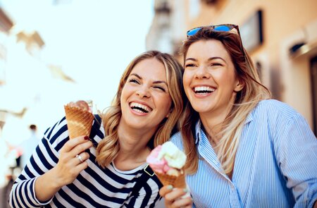 Zwei junge Frauen mit Eis in der Hand und lachen froehlich | © Gettyimages.com/djiledesign