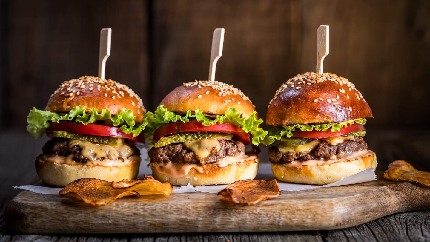 Leckerer Cheeseburger mit Salat, Cheddar-Kaese, Tomaten und Gurken. Burgerbroetchen mit Sesam. Rustikale Atmosphaere. Leckeres Fast-Food-Essen. | © Gettyimages.com/Haris Calkic, Edna Calkic