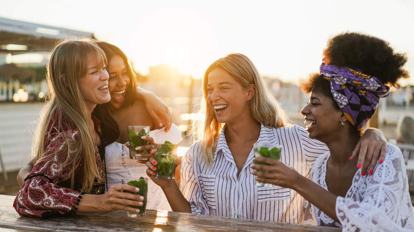 Glueckliche Maedchen, die Spass daran haben, Cocktails an der Bar am Strand zu trinken | © Gettyimages.com/disobeyart