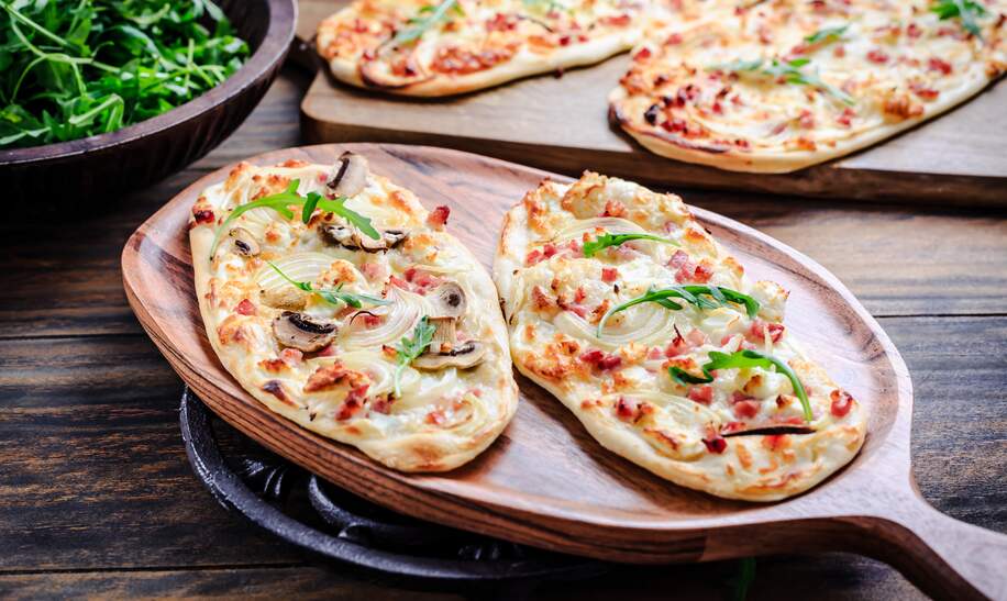 Franzoesischer Flammkuchen mit Frischkaese, Speck und Zwiebeln. Flammkuchen aus dem Elsass | © Gettyimages.com/brebca