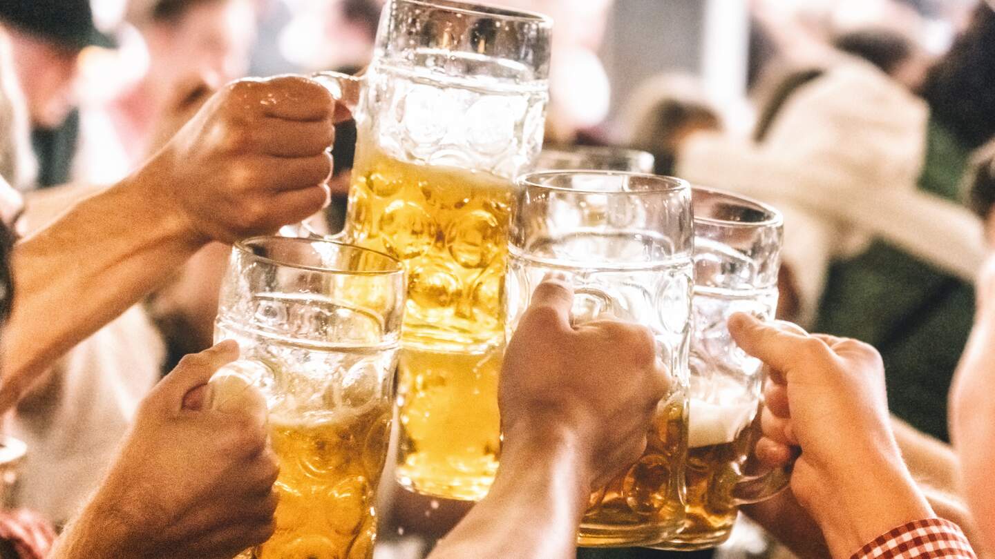 Händen heben große Maßkrüge aus Glas, gefüllt mit Bier, zum Anstoßen hoch | © GettyImages.com/polero