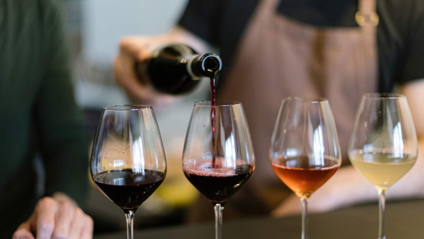Einschenken verschiedener Weine in die Glaeser, die für die Weinprobe auf der Theke arrangiert sind | © Gettyimages.com/Carlo Prearo