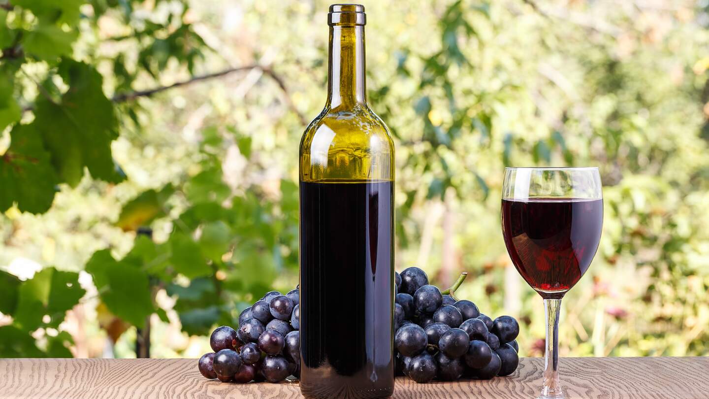 Flasche und ein Glas Wein mit Trauben auf einem hoelzernen Hintergrund im Freien | © Gettyimages.com/baronvsp