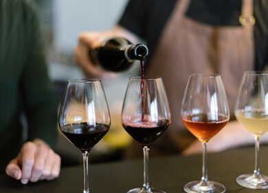 Einschenken verschiedener Weine in die Glaeser, die für die Weinprobe auf der Theke arrangiert sind | © Gettyimages.com/Carlo Prearo