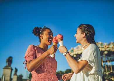 Zwei fröhliche, junge Frauen haben einen spaßigen Tag in Paris, Eis essend auf dem Rummel | © Gettyimages.com/Charday Penn