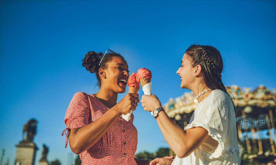 Zwei fröhliche, junge Frauen haben einen spaßigen Tag in Paris, Eis essend auf dem Rummel | © Gettyimages.com/Charday Penn