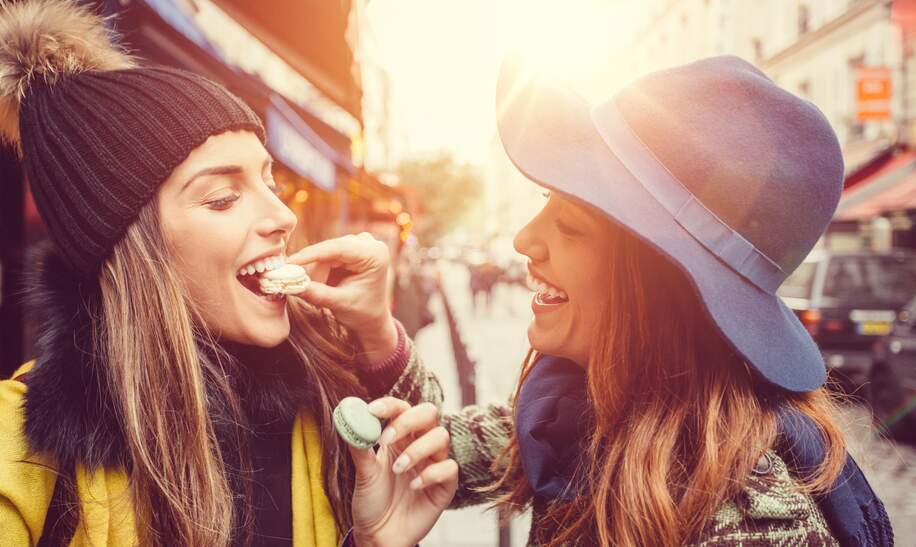 Zwei glückliche Frauen essen Macarons in Paris während einer Städtereise. | © Gettyimages.com/martin-dm