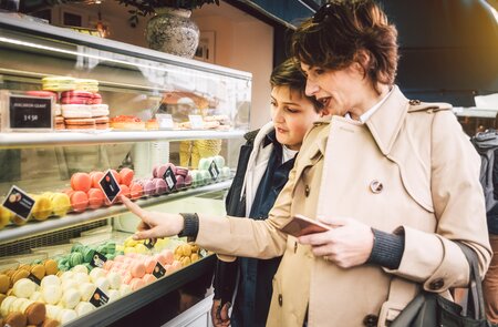 Französische Mutter und Sohn stehen am Stand in Paris und kaufen MAkaronen ein.  | © Gettyimages.com/Nikada