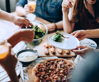Nahaufnahme einer jungen Gruppe fröhlicher Freunde, die Spaß daran haben, zusammen zu genießen, Essen über den Esstisch auf der Party zu verteilen und zu teilen | © © Gettyimages.com/AsiaVision