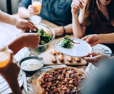 Nahaufnahme einer jungen Gruppe froehlicher Freunde, die Spass daran haben, zusammen zu genießen, Essen ueber den Esstisch auf der Party zu verteilen und zu teilen | © Gettyimages.com/AsiaVision