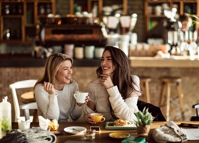 Zwei froehliche Frauen, die sich während der Kaffeezeit in einem Café vergnuegen.  | © Gettyimages.com/Drazen Zigic