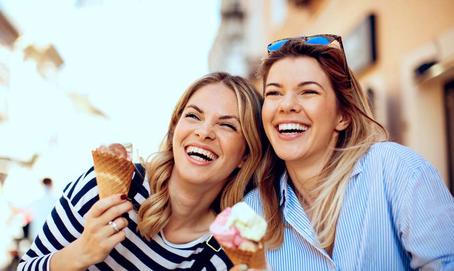 Zwei junge Frauen mit Eis in der Hand und lachen fröhlich | © Gettyimages.com/djiledesign