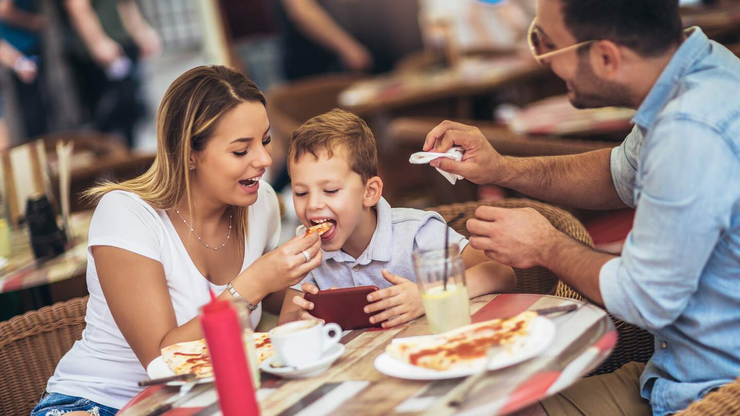 Mutter, Vater, Sohn essen in einem Restaurant Pizza | © Gettyimages.com/MandicJovan