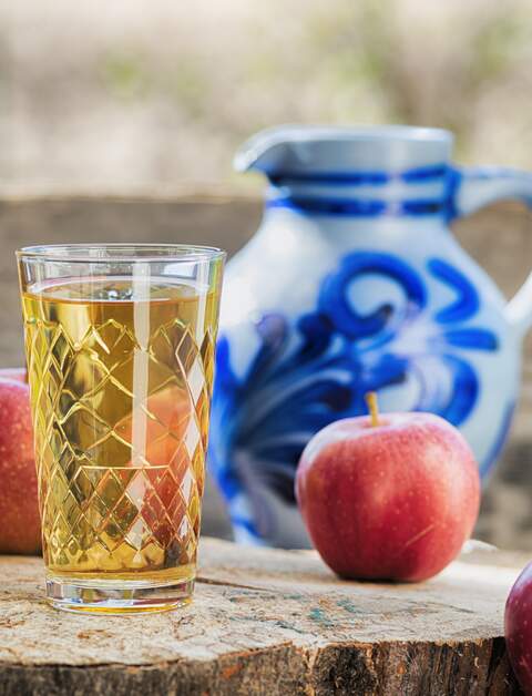 Traditioneller hessischer Apfelwein oder Apfelsaft vor dem traditionellen Tonkrug alias Bembel. Hoelzerner Hintergrund. | © Gettyimages.com/kontrast-fotodesign