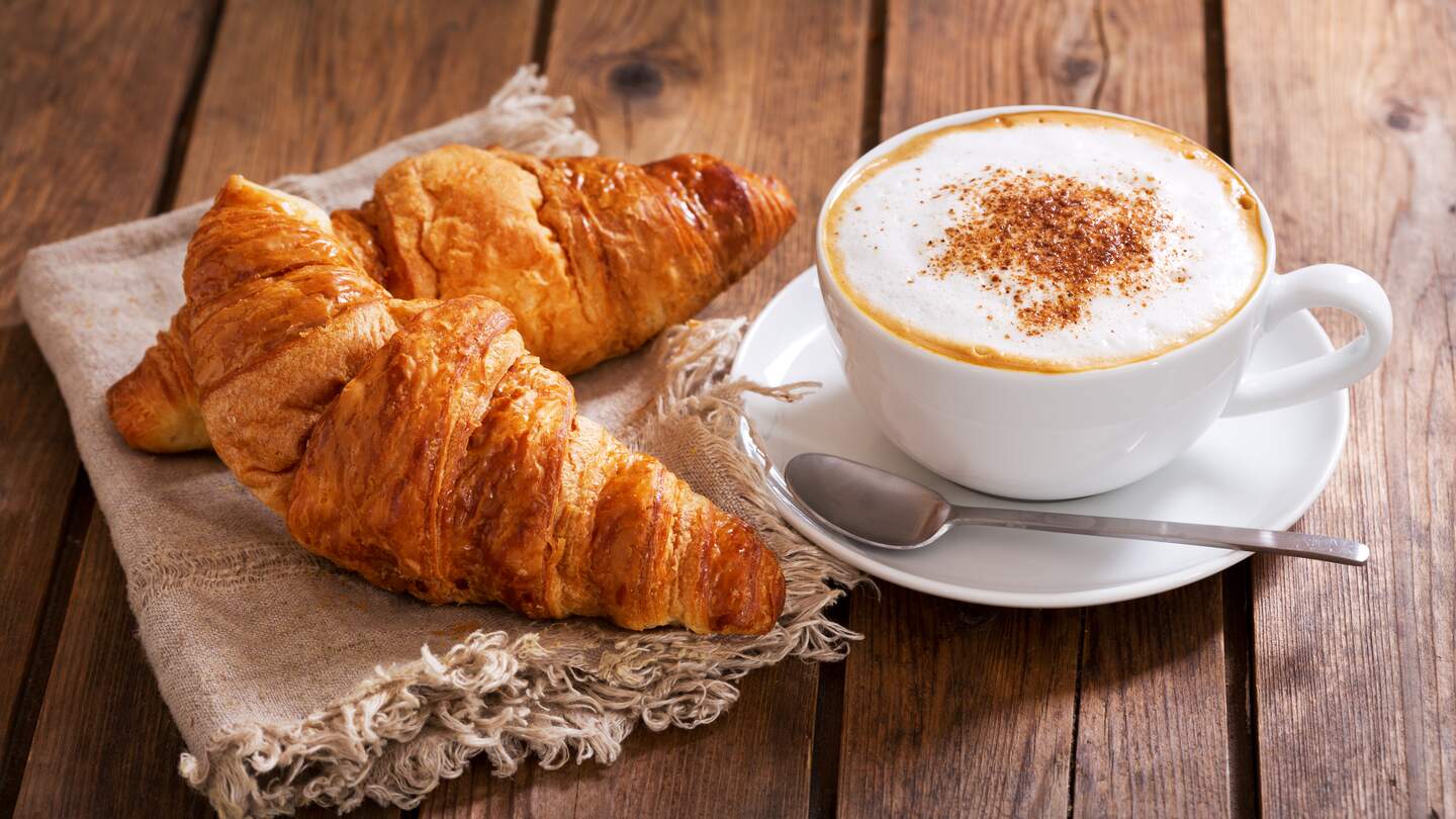 Tasse Cappuccino-Kaffee mit Croissants auf Holztisch | © Gettyimages.com/nitrub