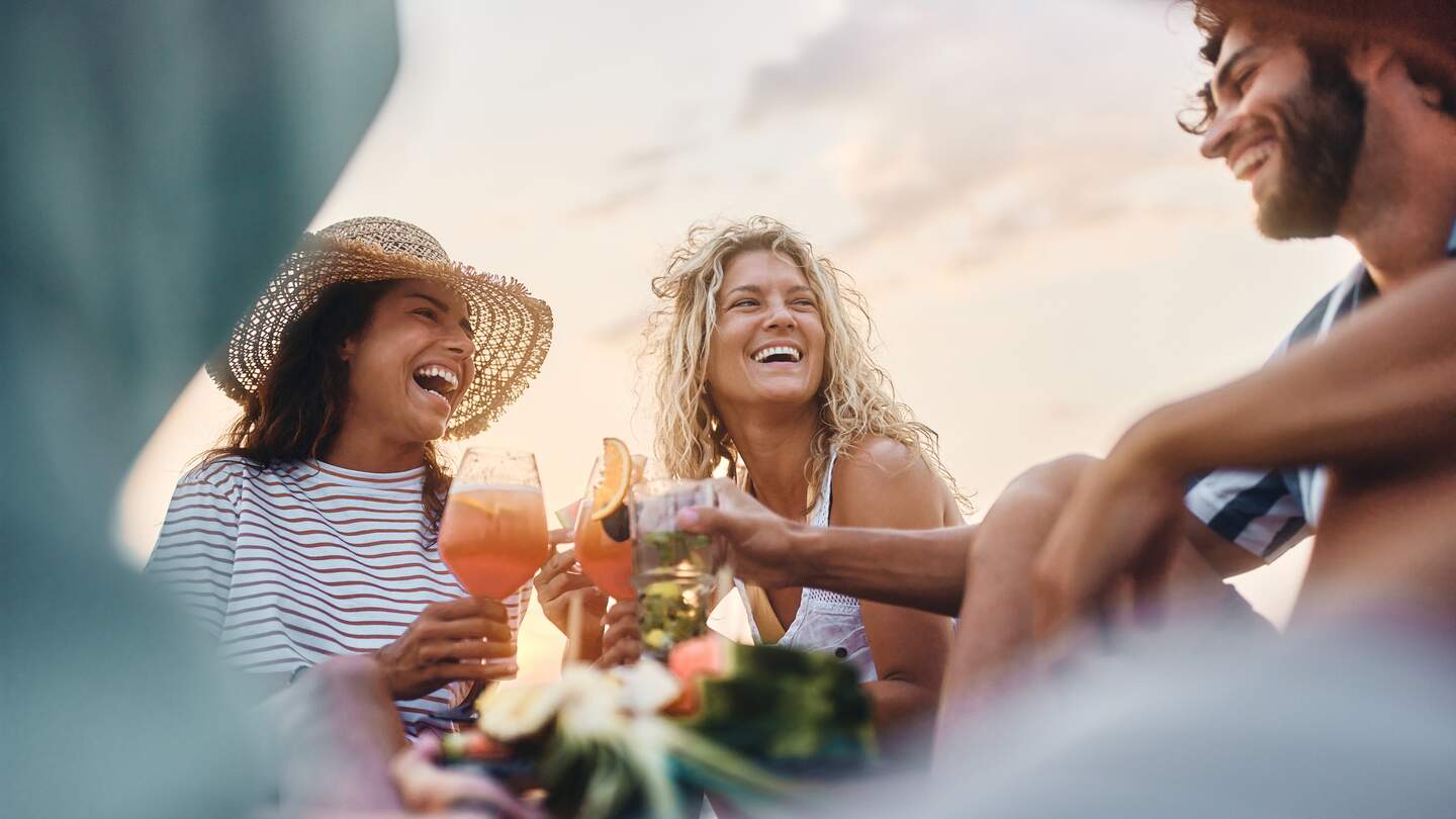 Niedrige Winkelansicht von gluecklichen Frauen, die mit ihrem maennlichen Freund am Sommertag anstossen. | © Gettyimages.com/skynesher