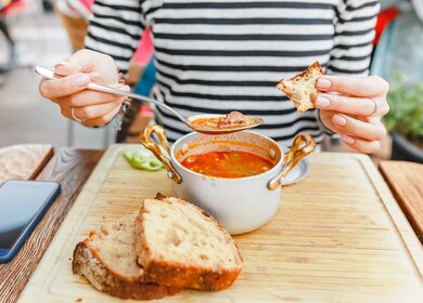 Eine Frau isst eine traditionelle ungarische Gulaschsuppe aus einem Topf in einem Restaurant im Freien | © Gettyimages.com/frantic00