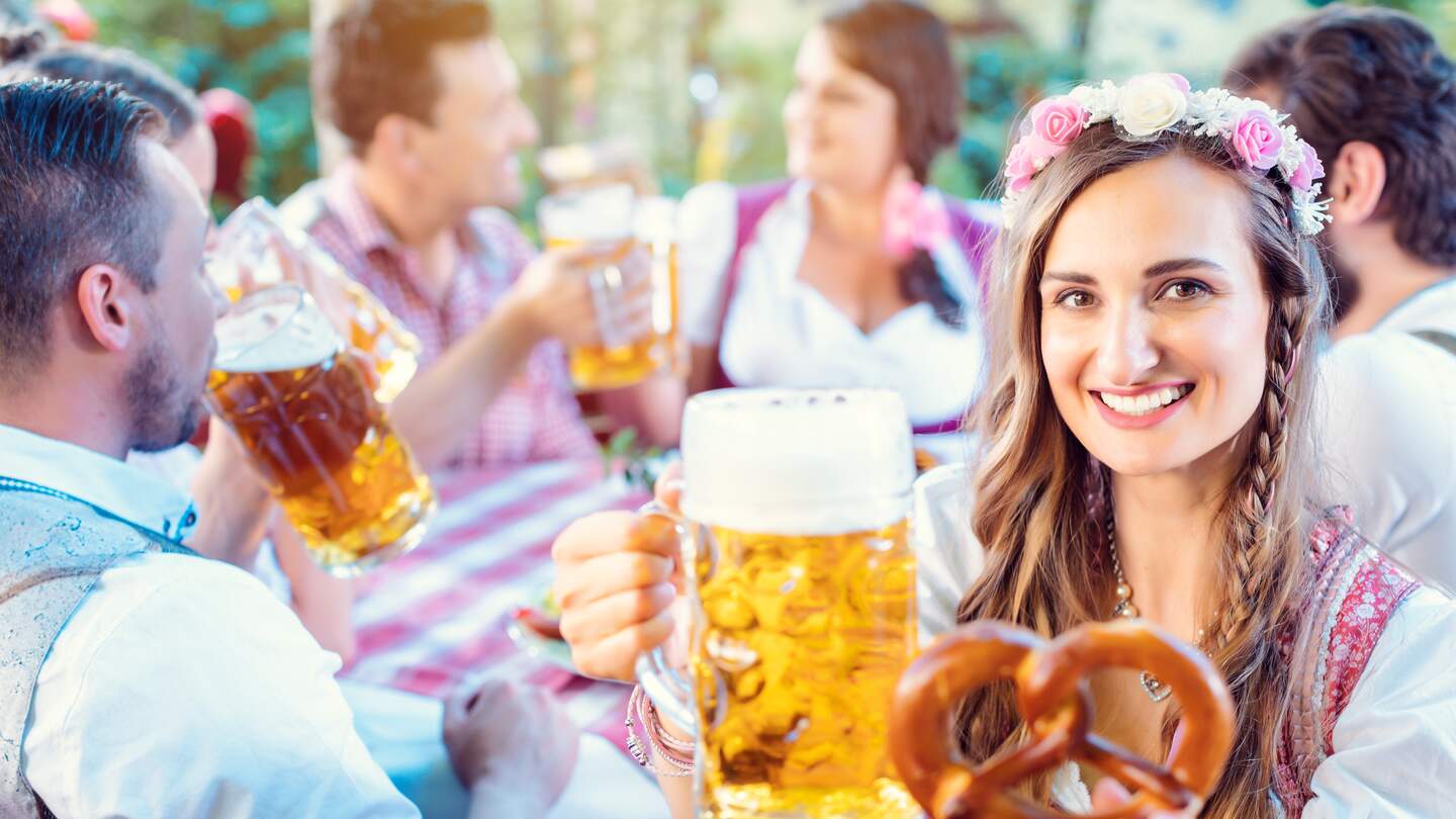 Frau toastet mit Glas Bier in bayerischer Kneipe in die Kamera  | © Gettyimages.com/kzenon