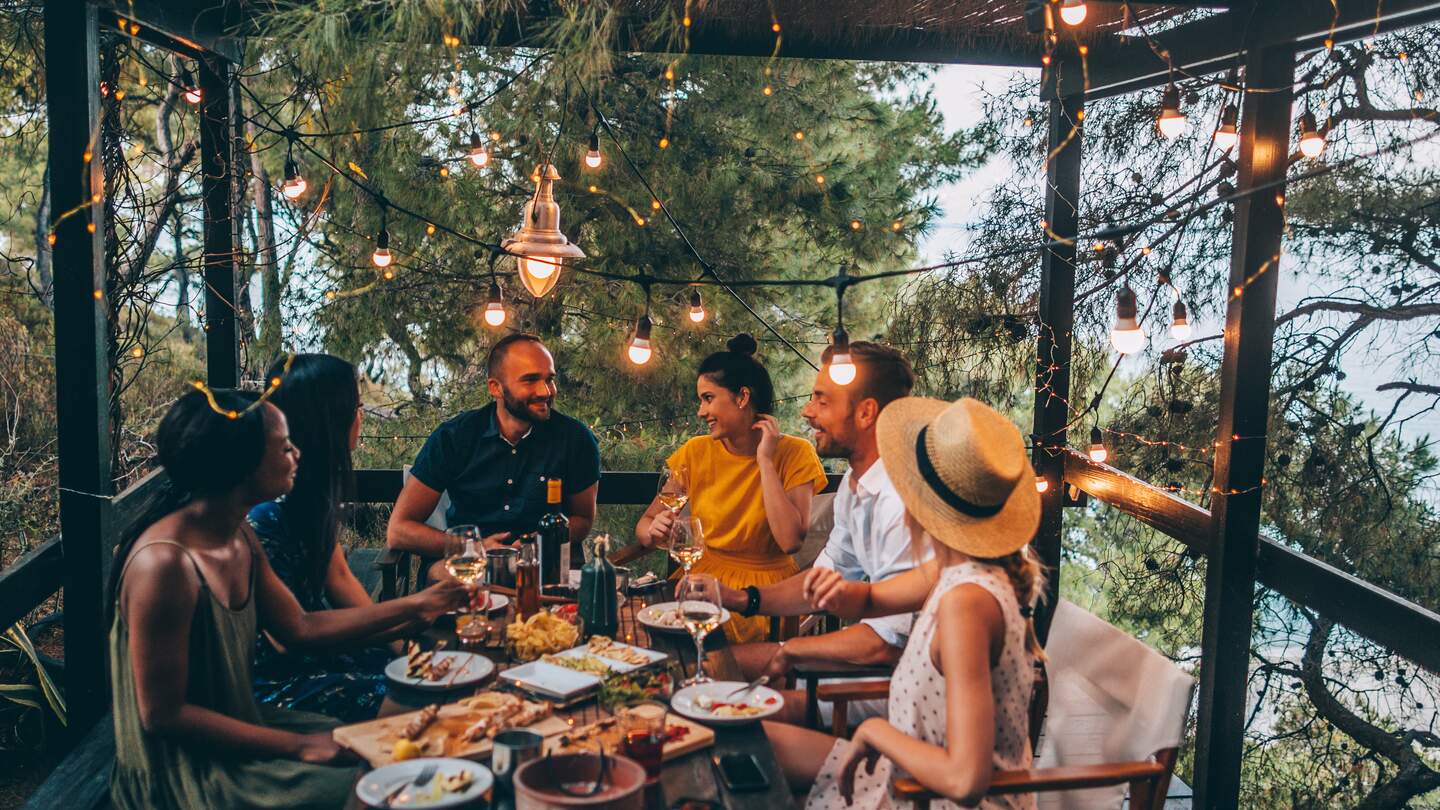 Eine Gruppe von Freunden veranstaltet eine Sommer-Dinnerparty auf der Terrasse | © Gettyimages.com/AleksandarNakic