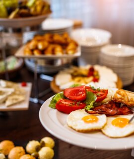 Frühstücksteller mit zwei Spiegeleiern und dem Restaurantbuffet im Hintergrund | © gettyimages.com/MilanEXPO