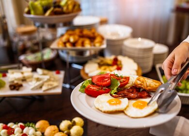 Frühstücksteller mit zwei Spiegeleiern und dem Restaurantbuffet im Hintergrund | © gettyimages.com/MilanEXPO