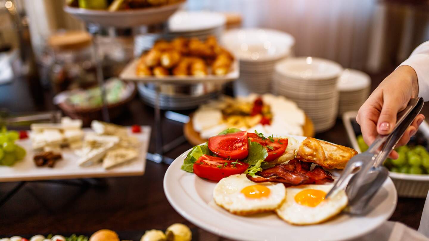 Frühstücksteller mit zwei Spiegeleiern und dem Restaurantbuffet im Hintergrund | © gettyimages.com/MilanEXPO