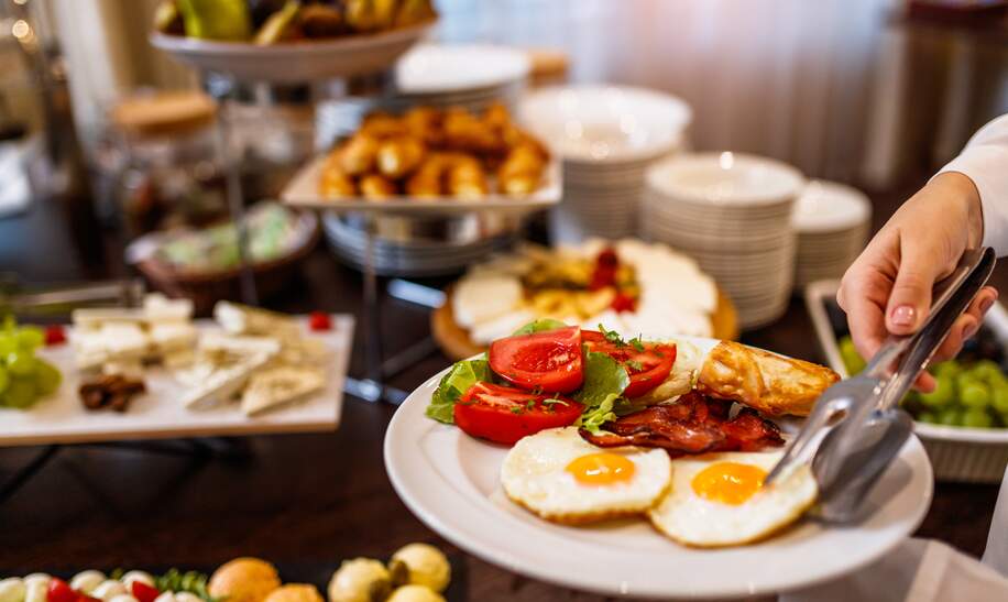 Frühstücksteller mit zwei Spiegeleiern und dem Restaurantbuffet im Hintergrund | © gettyimages.com/MilanEXPO