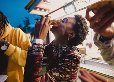 Eine junge Frau, die mit Freunden auf einem Musikfestival Pizza geniesst. | © Gettyimages.com/solstock
