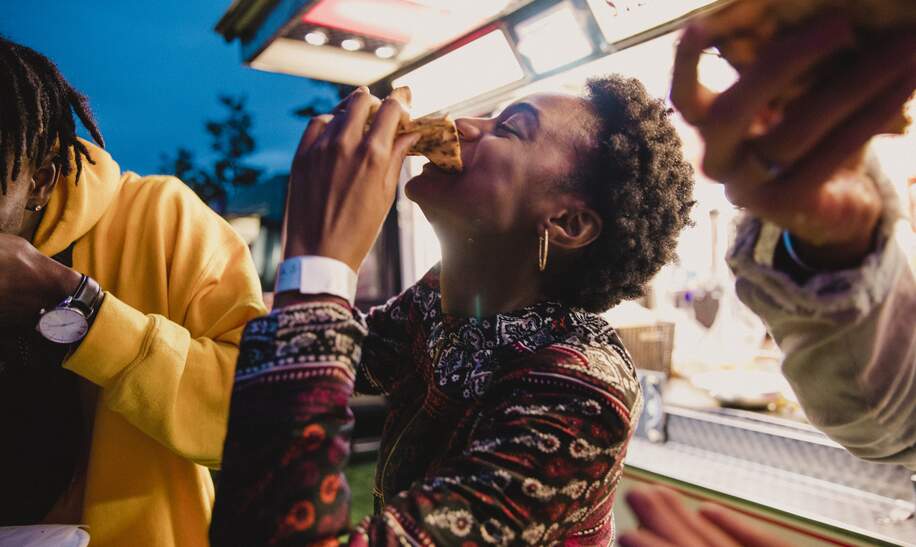 Eine junge Frau, die mit Freunden auf einem Musikfestival Pizza geniesst. | © Gettyimages.com/solstock
