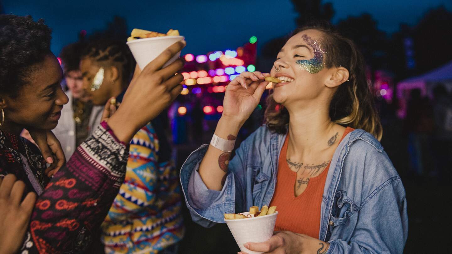 Zwei Freunde teilen sich Pommes auf einem festival | © Gettyimages.com/solstock