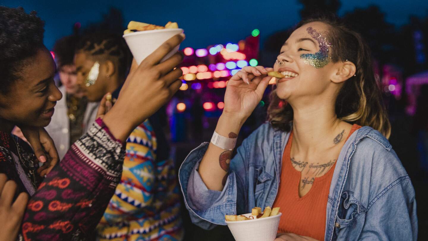 Zwei Freunde teilen sich Pommes auf einem festival | © Gettyimages.com/solstock