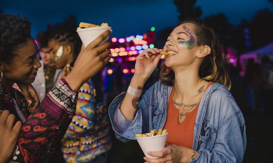 Zwei Freunde teilen sich Pommes auf einem festival | © Gettyimages.com/solstock