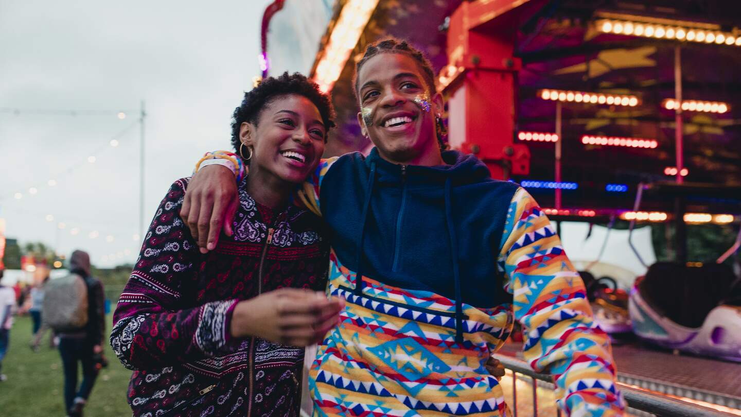 Ein junges Paar läuft lachend über eine Kirmes | © Gettyimages.com/solstock