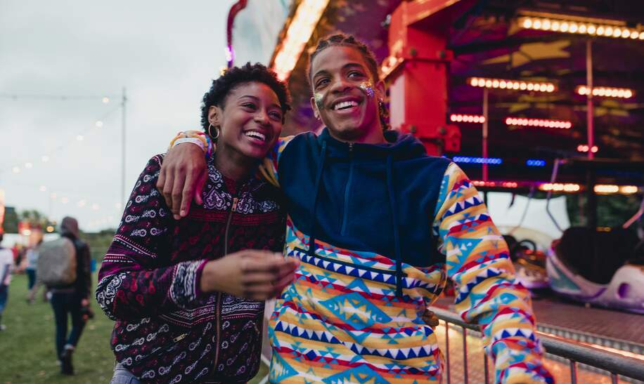 Ein junges Paar laeuft lachend ueber eine Kirmes | © Gettyimages.com/solstock