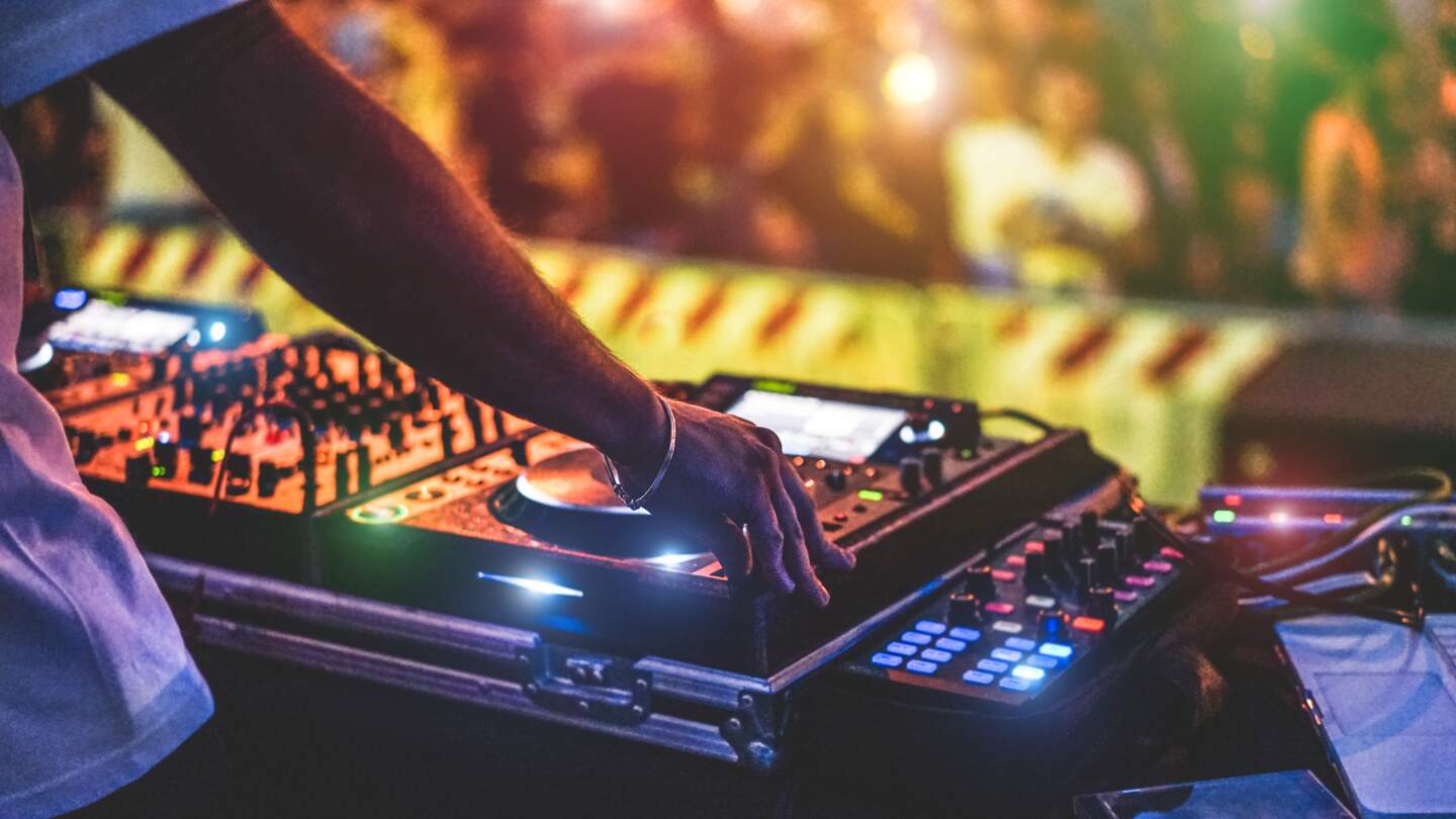 Dj Mixing Outdoor beim Silvester-Partyfestival mit Menschenmassen im Hintergrund | © Gettyimages.com/disobeyart