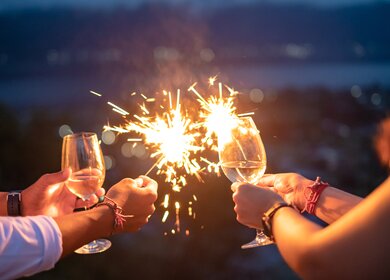 Gruppe von Freunden mit Wunderkerzen und Weißwein bei der Silvesterfeier | © Gettyimages.com/Kanawa_Studio