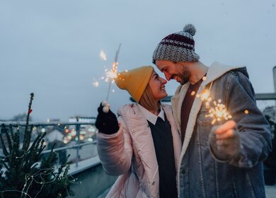 Junges Paar mit Wunderkerzen, die die schneereiche Silvesternacht zusammen geniessen. | ©  Gettyimages.com/AleksandarNakic