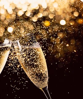 zwei Glaeser Champagner stossen in der Nacht mit Lichtern im  Glitzer und Funken im Hintergrund an | © Gettyimages.com/ASIFE