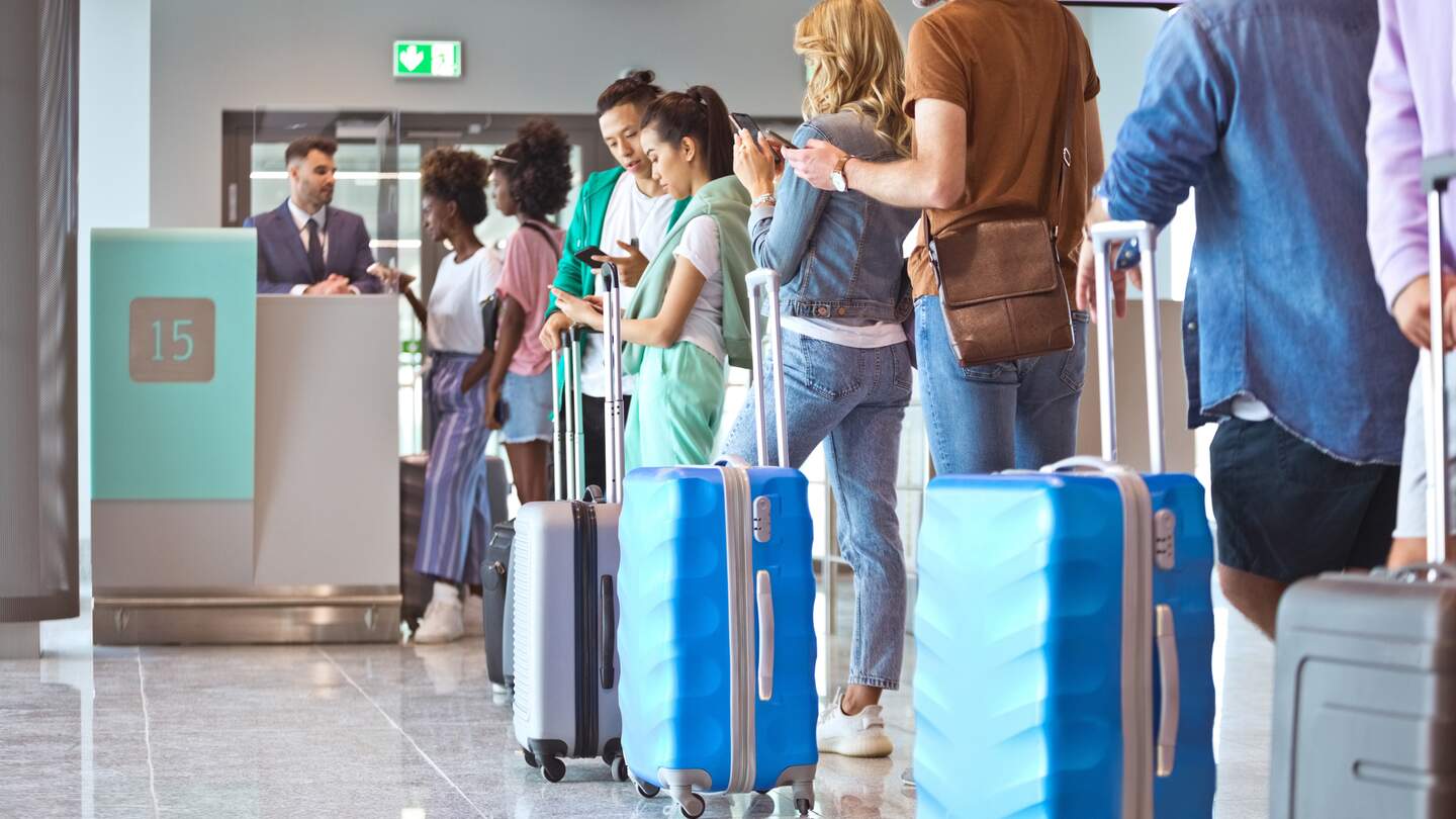 Passagiere mit Gepäck, die Smartphones benutzen, während sie am Flughafen in der Schlange stehen. | © GettyImages.de/izusek