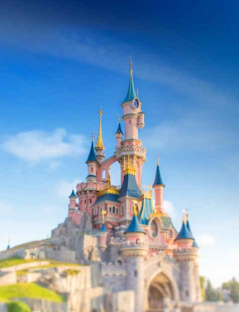 Das rosane Sleeping Beauty Castle mit blauen Tuermen, Fotografiert vom Central Plaza, umgeben von bunten Blumen. | © Disney