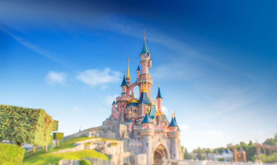 Das rosane Sleeping Beauty Castle mit blauen Tuermen, Fotografiert vom Central Plaza, umgeben von bunten Blumen. | © Disney