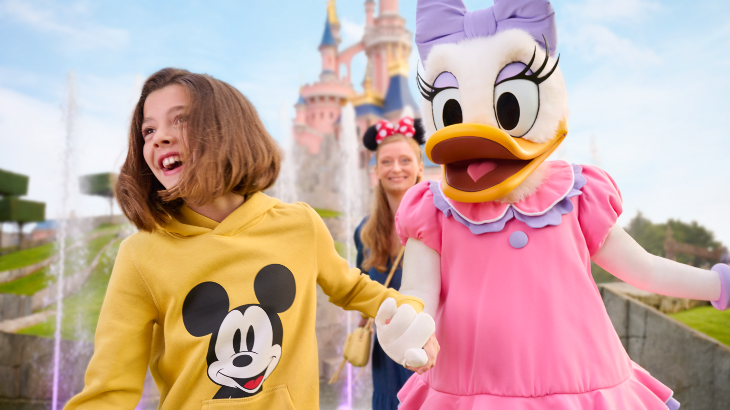 Daisy Duck und eine Frau mit Kind vor dem Sleeping Beauty Castle. | © Disney