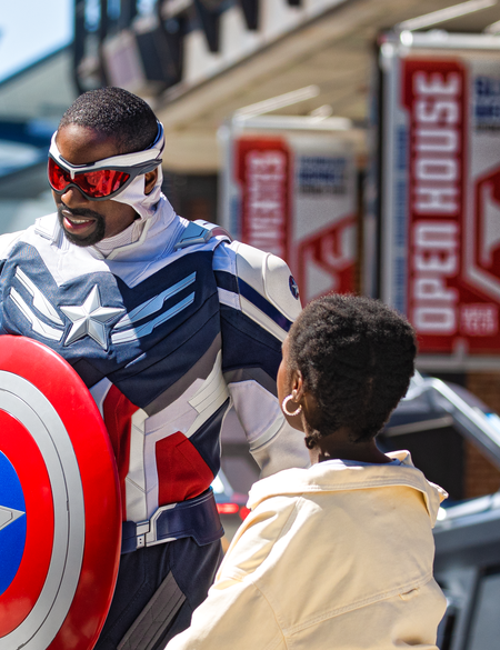 Walt Disney Studios Park Marvel Avengers Campus Captain America (Sam) mit seinem Schild und zwei Kindern, im Hintergrund der Quinjet | © 2024 MARVEL.