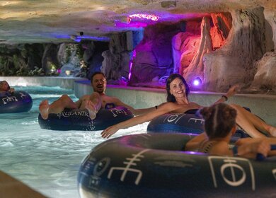 Gäste treiben entspannt auf Reifen durch eine farbenfroh beleuchtete Felsenlandschaft der Snorri Saga Wasserrutsche in der Wasserwelt Rulantica im Europa‑Park. | © Europa-Park Erlebnis-Resort