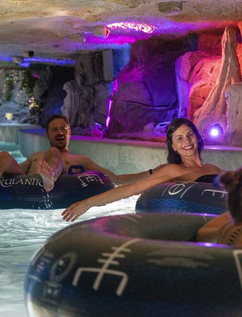 Gäste treiben entspannt auf Reifen durch eine farbenfroh beleuchtete Felsenlandschaft der Snorri Saga Wasserrutsche in der Wasserwelt Rulantica im Europa‑Park. | © Europa-Park Erlebnis-Resort