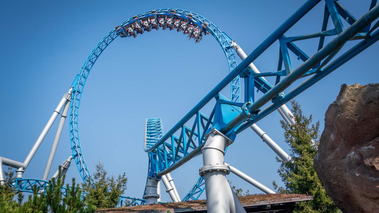 Blaue Achterbahn fährt mit hoher Geschwindigkeit durch einen großen Looping, während Fahrgäste den Adrenalinkick unter klarem Himmel über grüner Landschaft genießen. | © Europa-Park