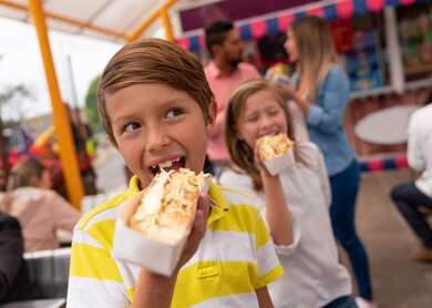 Kinder essen Hotdogs auf einem Festplatz | © gettyimages.com/andresr