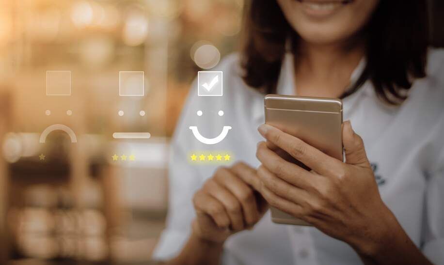 Geschäftsfrau, die Gesichtsemoticon auf dem virtuellen Touchscreen am Smartphone drückt.  | © Gettyimages.com/Urupong