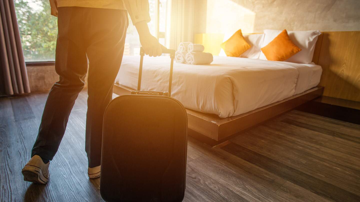Mann mit seinem Koffer in einem Hotelzimmer vor dem Bett | © GettyImages.com/Boyloso