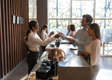 Gruppe von Menschen, die Check-in im Hotel und freundliche Recepcionist helfen Ihnen | © Gettyimages.com/Hispanolistic